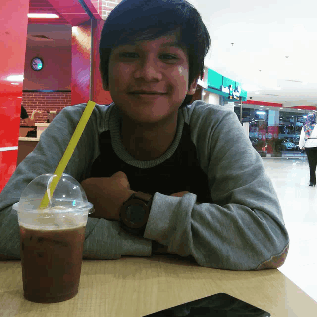 a young man is sitting at a table with a cup of coffee and a straw