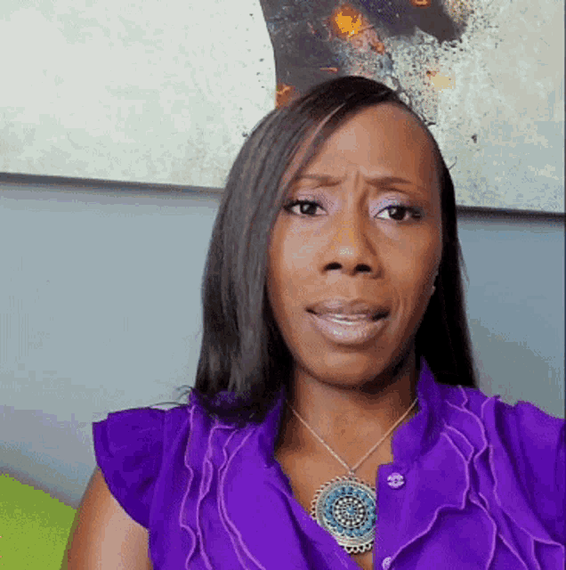 a woman wearing a purple shirt and a necklace makes a funny face