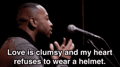 a man singing into a microphone with the words love is clumsy and my heart refuses to wear a helmet below