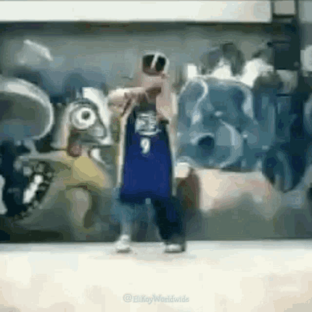 a person is standing in front of a graffiti wall wearing a blue jersey and sunglasses .
