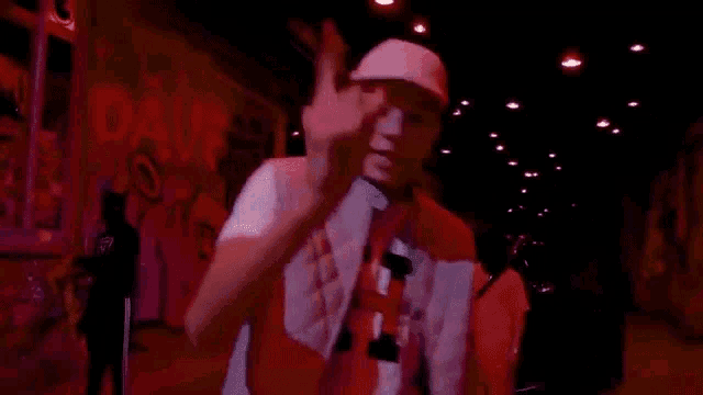 a young man wearing a hat and a vest is standing in front of a graffiti wall .