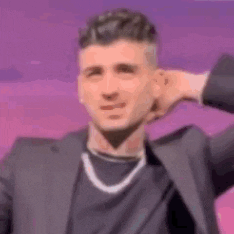 a man wearing a suit and a necklace is covering his ears with his hand .