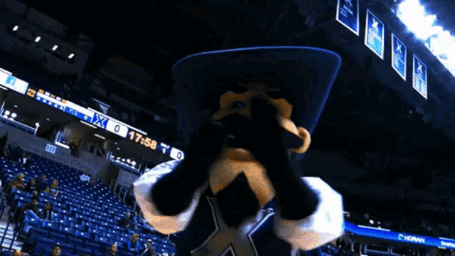 a mascot with a cowboy hat and a mustache stands in front of a sign that says horns