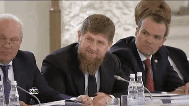 a man with a beard is sitting at a table with other men and a bottle of water
