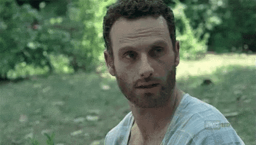 a man with a beard is wearing a blue shirt and standing in a field .
