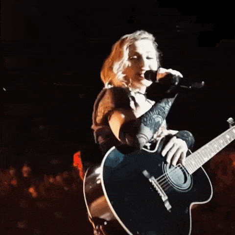 a woman is playing a guitar and singing into a microphone on stage .