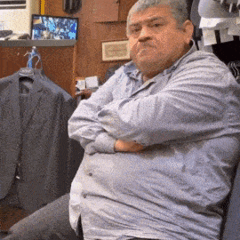 a man with his arms crossed is sitting in front of a wall with clothes hanging on it