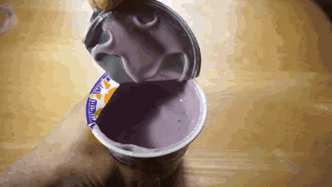a person is opening a container of purple yogurt with a spoon .