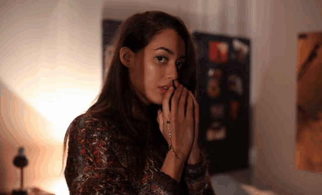 a woman covering her face with her hands in front of a wall with pictures