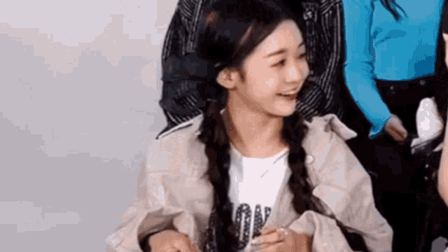 a young girl with pigtails is smiling while sitting in a room with other people .