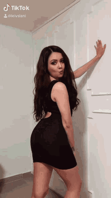 a woman in a black dress is standing in front of a wall .