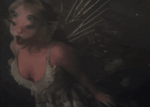 a woman with three eyes and wings looks up at the camera