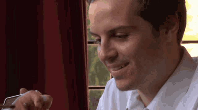 a man in a white shirt is smiling while looking at his cell phone