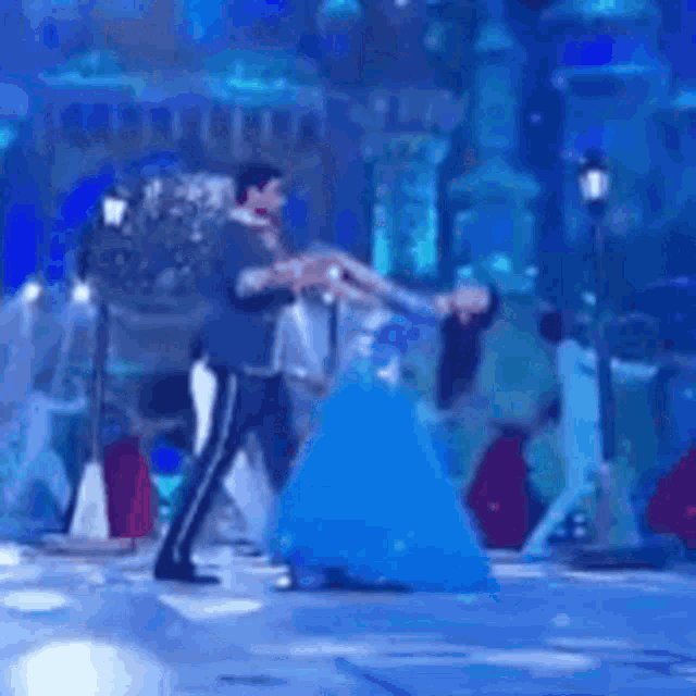 a man and a woman are dancing together on a stage . the woman is wearing a blue dress .