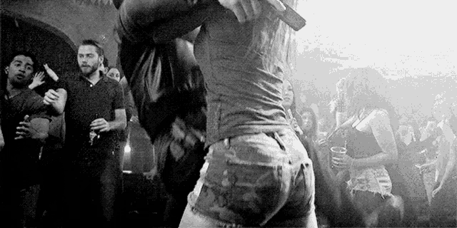 a black and white photo of a woman dancing in front of a crowd of people in a club .