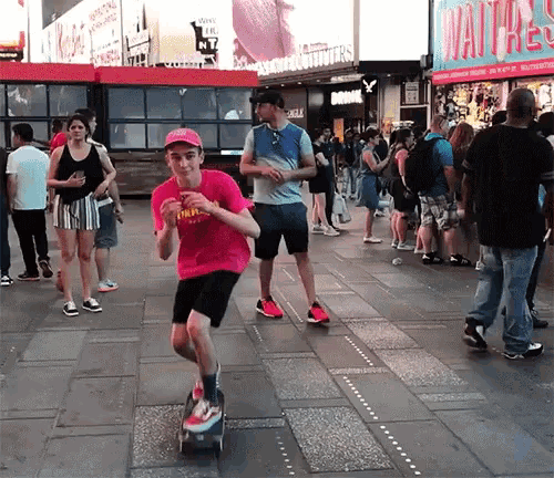 a boy in a pink shirt is riding a skateboard on a street