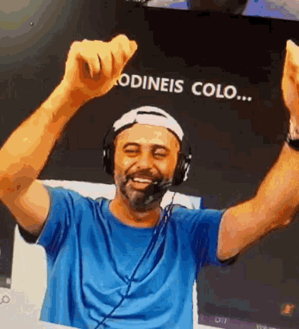a man wearing headphones and a blue shirt holds his arms up in the air