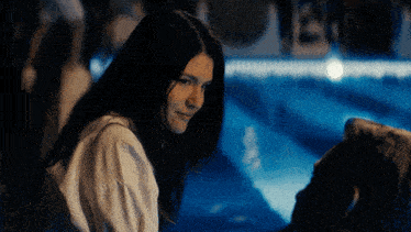 a woman in a white shirt sits next to a man in front of a pool