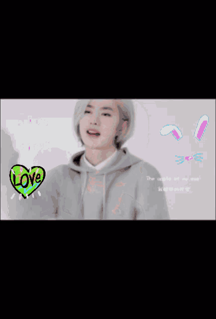 a man in a grey hoodie has a pink heart with the word love on it