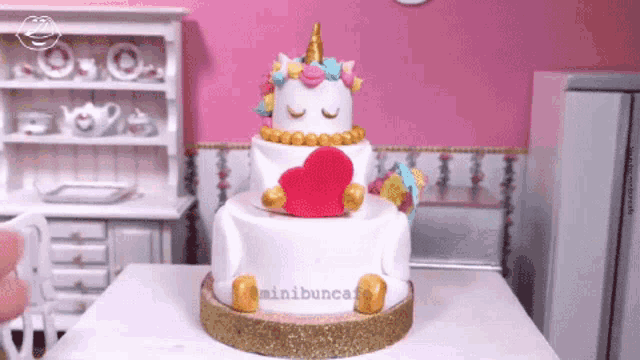 a unicorn cake with a heart on top is on a table with minibuncare written on it