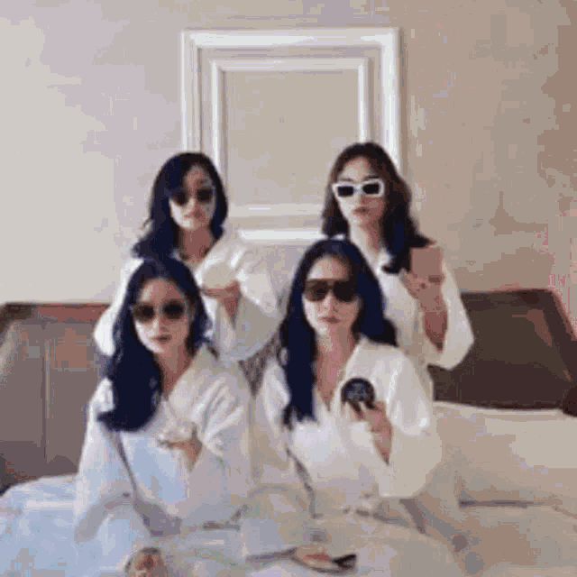 a group of four women wearing bathrobes and sunglasses are sitting on a bed .