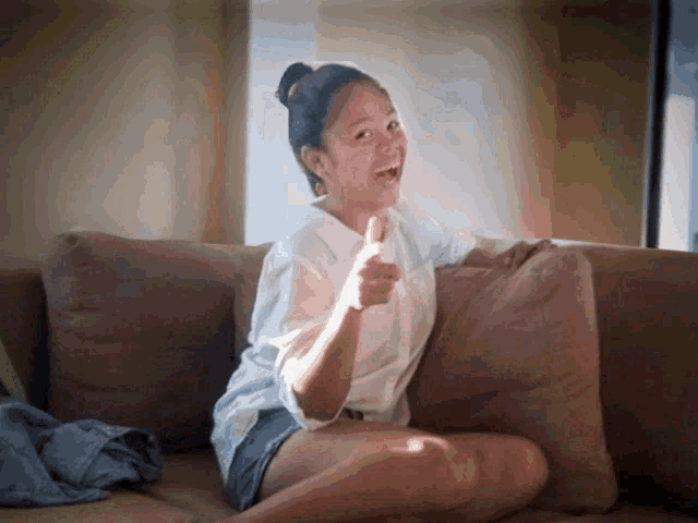 a woman sitting on a couch giving a thumbs up sign