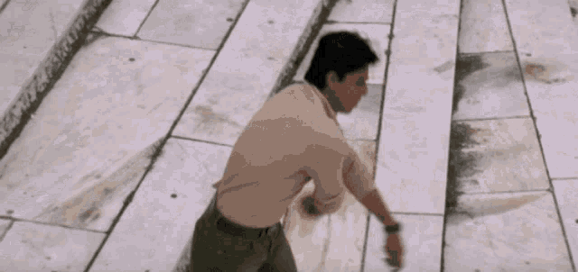 a man in a tan shirt is standing on a tiled floor with his arms outstretched