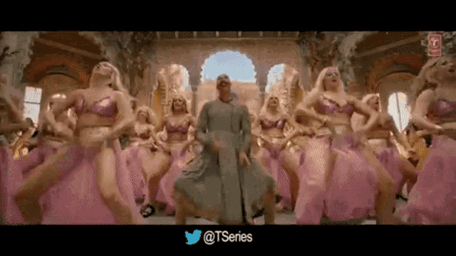 a group of women are dancing in a room with a man in a green dress .