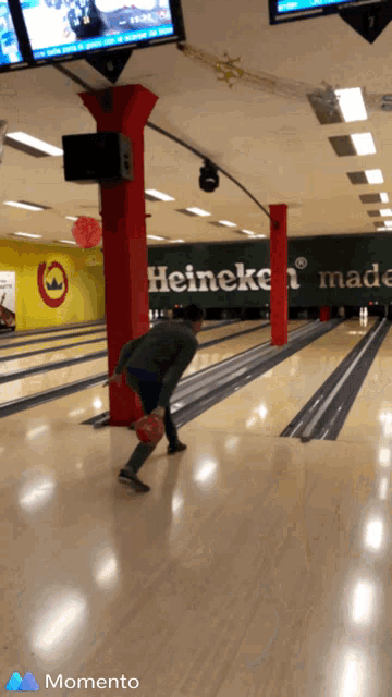 a man is bowling in a bowling alley with a heineken sign behind him