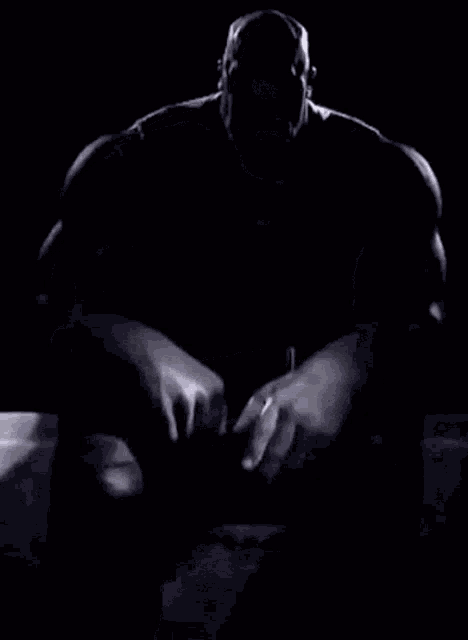 a bald man with a beard is sitting down with his hands folded .