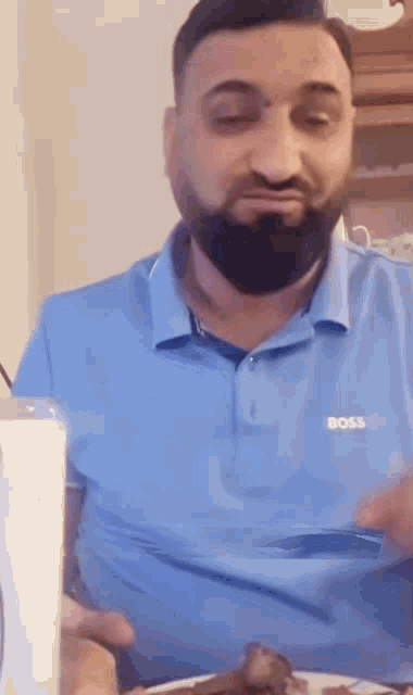 a man with a beard is wearing a blue shirt and eating a plate of food .