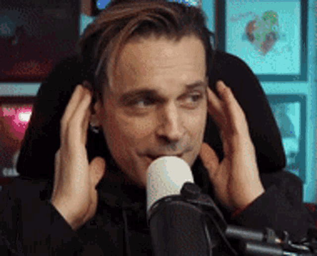 a man is sitting in front of a microphone covering his ears .