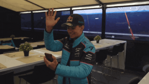 a man wearing a red bull hat waves at someone