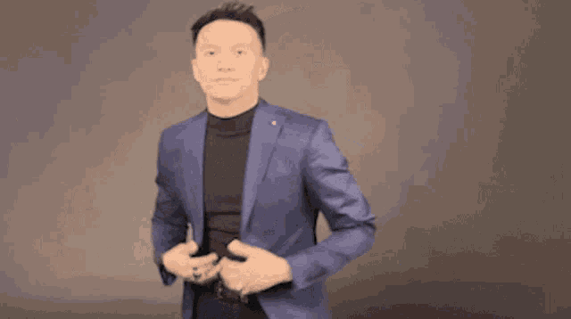 a man in a blue jacket and black turtleneck shows off his jacket