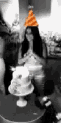 a blurry photo of a woman wearing a party hat and a cake on a table .
