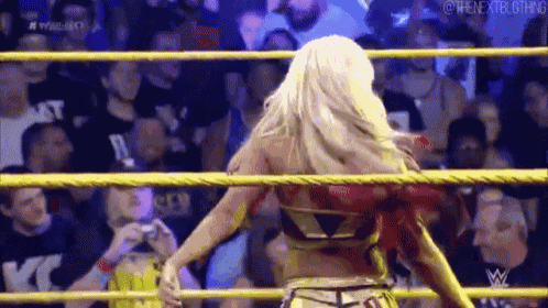 a woman is standing in a wrestling ring with a crowd of people watching .