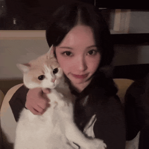 a woman is holding a white and brown cat
