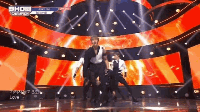 a group of men are dancing on a stage with a large screen behind them .