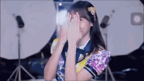 a woman is covering her face with her hands while standing in front of a camera .