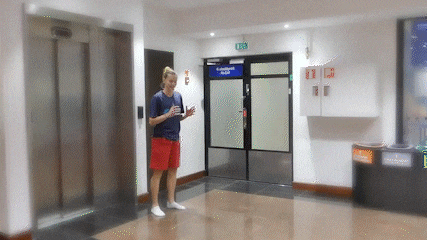 a woman is standing in front of a blue door that says ' emergency exit ' on it