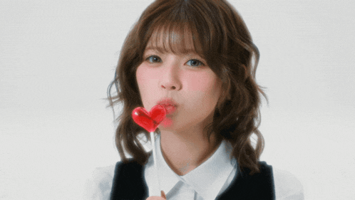 a woman with a heart shaped lollipop in front of her face