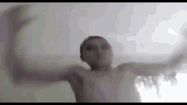 a shirtless man is standing in front of a window with his arms outstretched in a blurry photo .