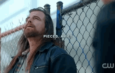 a man with long hair is standing next to a chain link fence .