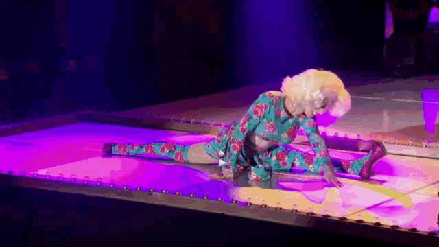 a drag queen is doing a split on a stage while wearing a floral dress .