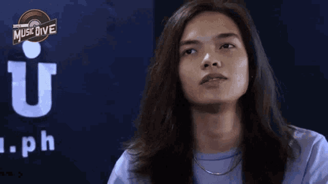 a man with long hair is wearing a purple shirt and looking at the camera .