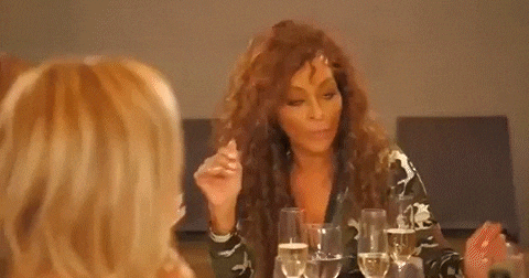 a woman is sitting at a table with glasses of wine and laughing .