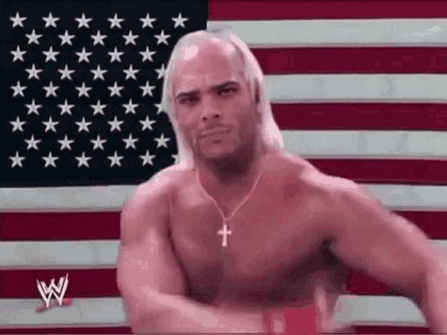 a shirtless wrestler with a cross necklace is standing in front of a flag .
