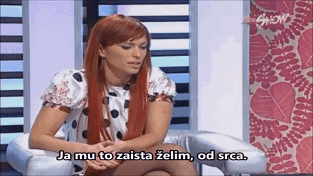 a woman with red hair is sitting in a chair with the words " ja mu to zaista zelim od srca " above her