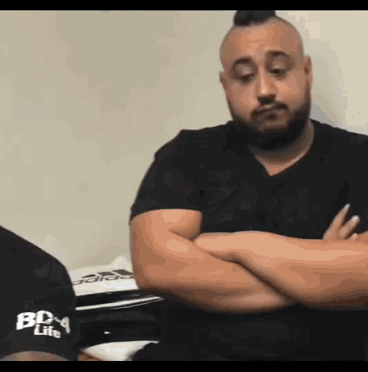 a man with a mohawk is sitting with his arms crossed and wearing a black shirt that says box life