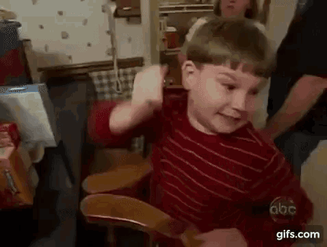 a young boy in a red striped shirt is sitting in a wooden chair .